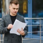 Portrait of serious businessman looking papers on city street. Worried manager reading documents in stylish suit outside. Disappointed executive working with documents outdoors